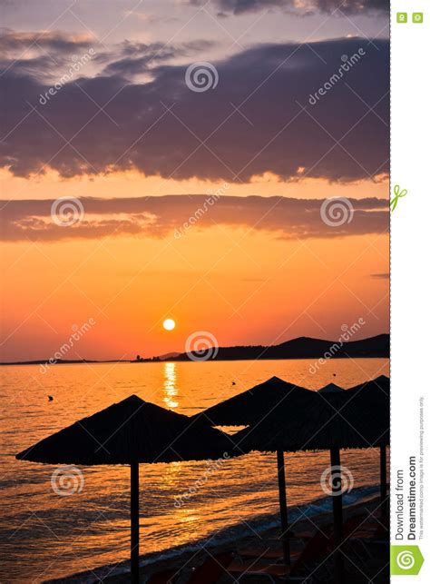 Sandy Beach With Stray Sunshades And Orange Chairs At Sunset In