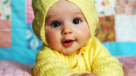 Cute Baby Is Wearing Yellow Knitted Wool Dress Lying Down On Bed In A