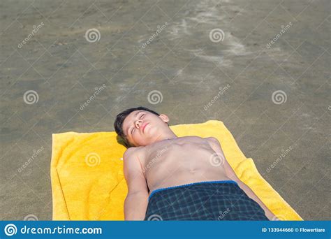Teen Boy Lies On Yellow Towel And Sunbathes On The Beach On The Sea And
