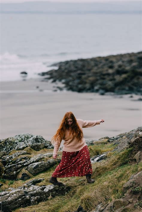 A Young Woman With Ginger Hair Climbing Along A Verge Near A Beach In