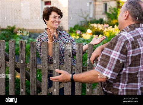 Neighbors Man And Woman Chatting Near The Fence In The Village Stock