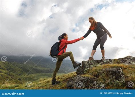 Girls Helping Each Other Hike Up A Mountain At Sunrise Giving A Stock