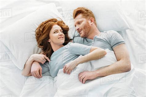 Happy Redhead Couple Smiling Each Other While Sleeping Together In Bed