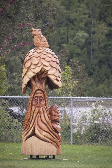 A Wooden Carving Of A Bird Sitting On Top Of A Tree Stump In The Grass