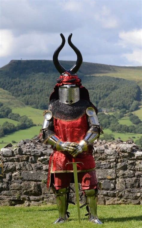 A Man Dressed In Armor Standing On Top Of A Lush Green Field Next To A