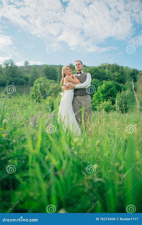 The Bride And Groom With A Bouquet In The Grass Against The Background