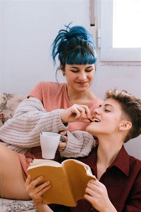 Lesbian Couple Having Breakfast And Reading On A Retro Sofa In A White
