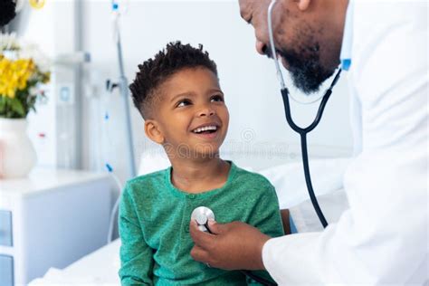 African American Male Doctor Using Stethoscope On Smiling Boy Patient