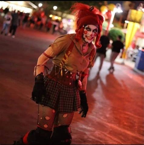 A Woman Dressed Up As A Clown Walking Down The Street At Night With Other People In The Background