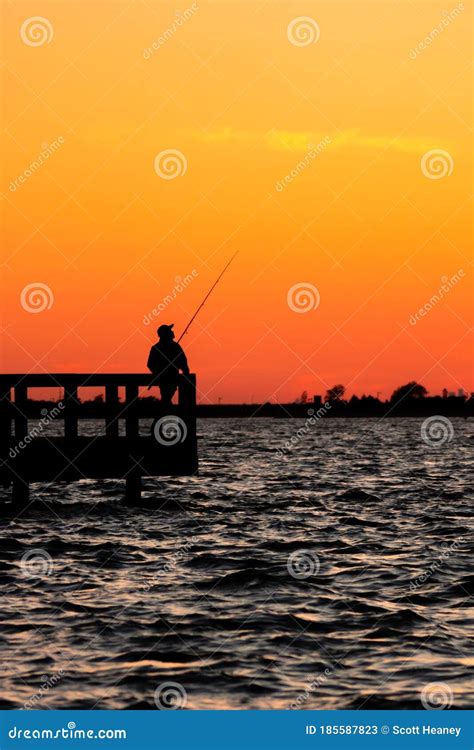 Silhouette Of A Fisherman Standing Alone On A Fishing Pier Under A
