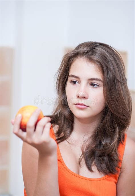 Девочка подросток в оранжевой футболке думая и держа персик в ее руке Стоковое Изображение