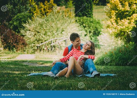 Young Loving Couple Is Sitting On A Plaid In The Park Hugging Fooling