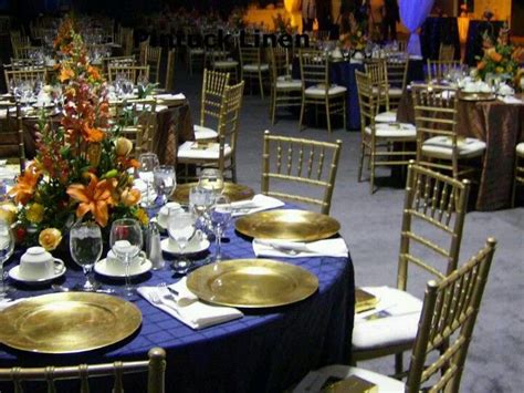 A colorful wedding barn table with coral blooms and napkins, tall and thin candles and navy napkin rings and stools. Navy & Gold table setting | Gold table setting, Gold table ...