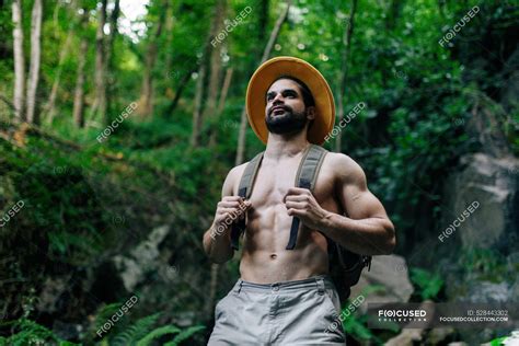 d en bas du voyageur homme torse nu avec sac à dos et chapeau debout dans les bois rocheux et