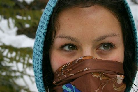 A Woman Wearing A Scarf Around Her Face With Snow In The Back Ground Behind Her