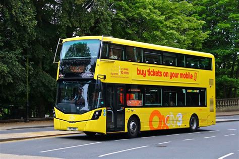 A Yellow Double Decker Bus Is Driving Down The Street With Trees In The