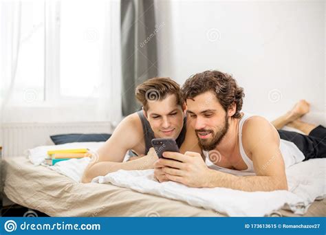 Cute Caucasian Gay Couple On Bed Use Smartphone Stock