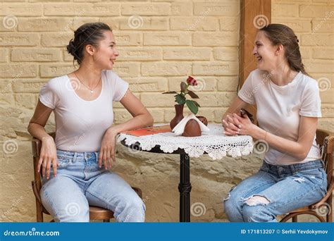 Two Young Women Sitting At Table In Cafe And Talk Small Talk Gossip