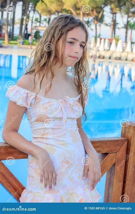 cute teen girl in a romantic dress and with long hair is standing on the bridge by the pool