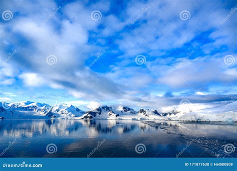 Antarctic Landscape With Snow Capped Mountains Reflecting In Dark Blue