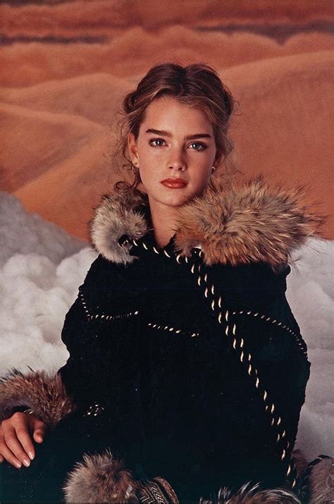 A Woman Sitting In The Snow Wearing A Black Coat With Fur Collar And