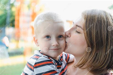 Mother Hugs And Kissing Her Baby Boy On The Park Motherhood Young