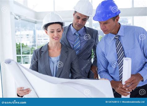 Businessmen And A Woman With Hard Hats And Holding Blueprint Stock