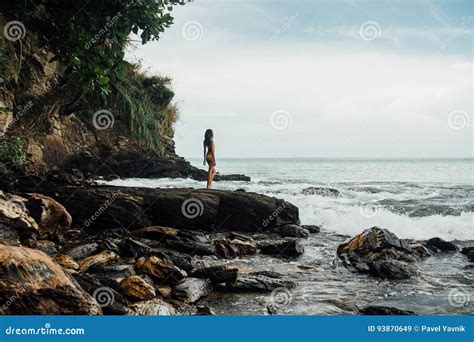 Beautiful Young Woman In Yellow Bikini Standing On A Rock On Ocean