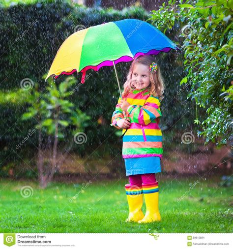 Little Girl Playing In The Rain Under Colorful Umbrella Stock Photo