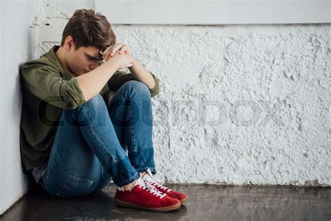 Sad Teenager In Jeans Holding Smartphone And Sitting On Floor Stock