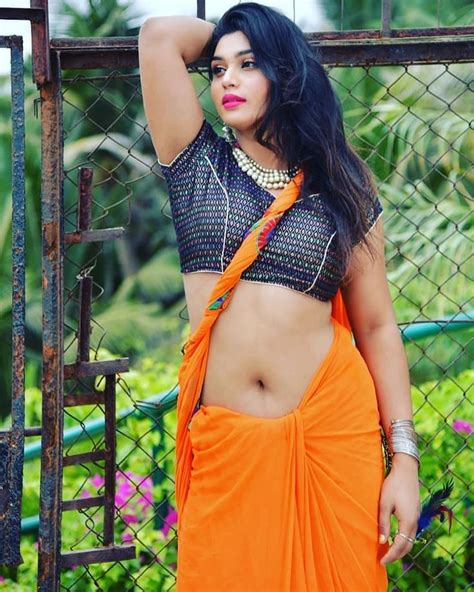 A Woman In An Orange Sari Posing By A Fence With Her Hand On Her Head