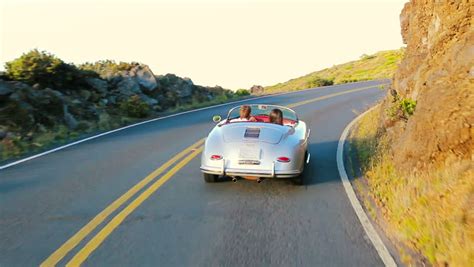 Happy Couple Driving Classic Convertible Car Into Sunset On Country