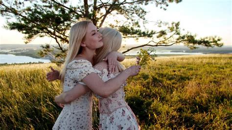 A Blonde Girl Gives Her Girlfriend Flowers Standing In A Field And They