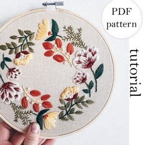 A Hand Is Holding Up A Embroidery Hoop With Flowers On It And The Words