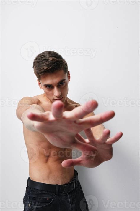 A Man With A Naked Torso Gestures With His Hands In Front Of His Face Against A Light Background