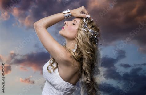 greek goddess blond woman with silver laurel wreath dressed in white silks in the wind sunset