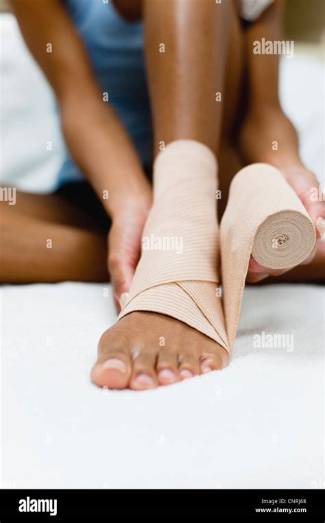 Woman Wrapping Bandage Around Injured Ankle Low Section Stock Photo