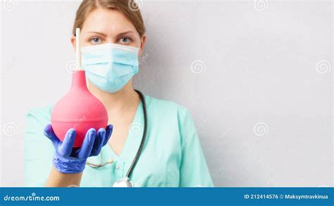 Nurse Doctor With Enema In Hand A Woman In A Medical Uniform And A Protective Mask Holds An