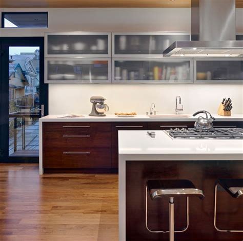 Stainless steel kitchen cabinets are located beneath stacked frosted glass cabinets flanked by stainless steel refrigerators placed under stainless steel frosted glass china cabinet doors open to stainless steel shelves and are fixed above stainless steel cabinets, under frosted glass overhead. A Mix Of Functionality And Style In The Form Of Glass Kitchen Cabinets