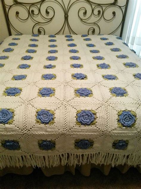 crocheted bedspread granny squares with 3 layer blue flowers and green trim has fringe on 3