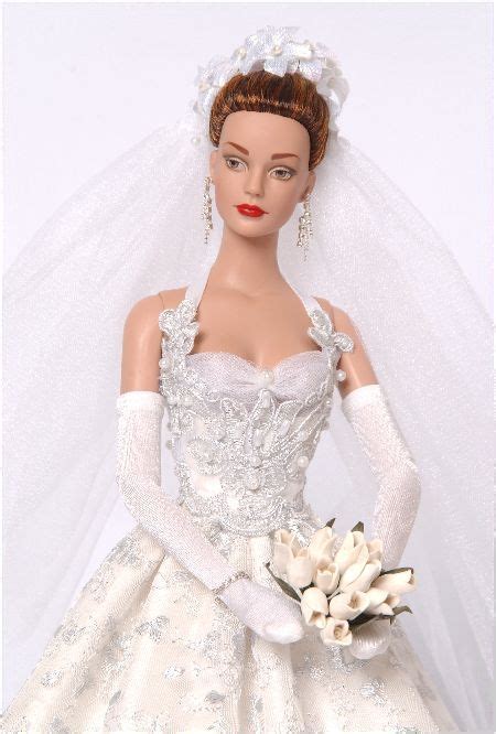 a doll wearing a wedding dress and veil with flowers in her hair is holding a bridal bouquet