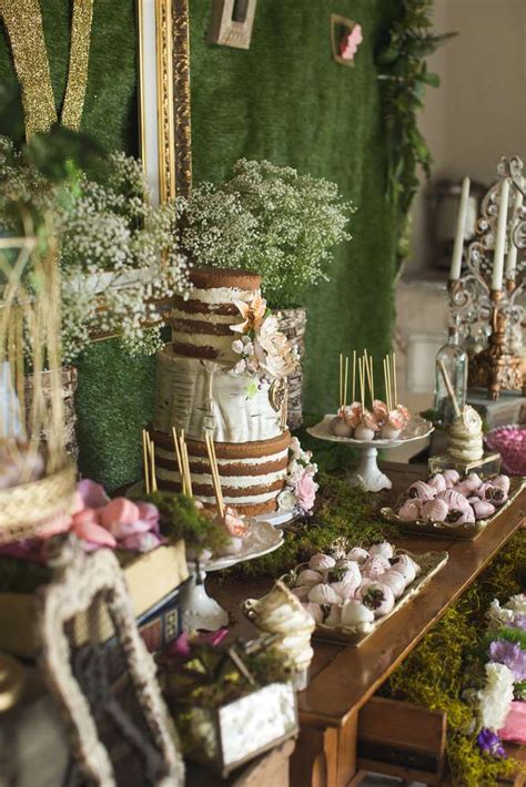 A Table Topped With Lots Of Desserts Next To A Wall Covered In Greenery