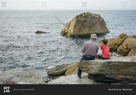 Grandfather And Grandson Fishing Together At The Sea Sitting On Rock