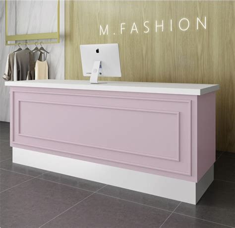 A Pink And White Reception Desk In Front Of A Wall With Clothes Hanging