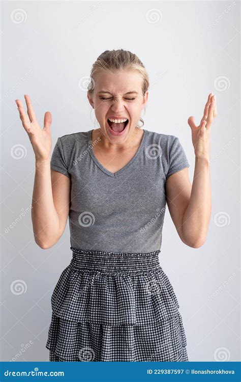 Portrait Of Woman Screaming In Despair Standing By Gray Wall Stock
