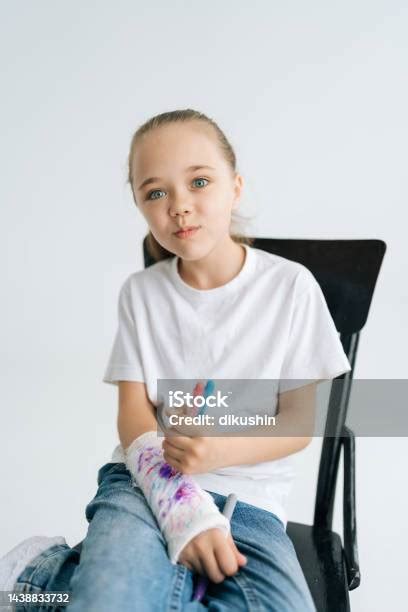 카메라를 바라보는 흰색 석고 붕대로 싸인 부러진 팔에 다채로운 마커가 있는 귀여운 이미지를 그리는 긍정적인 어린 소녀의 수직