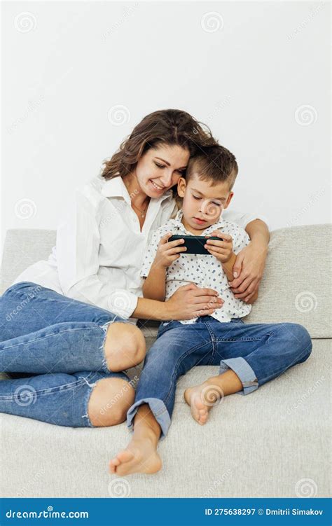 Mother And Baby Playing With A Smart Phone Sitting On A Couch In The Living Room At Home Stock