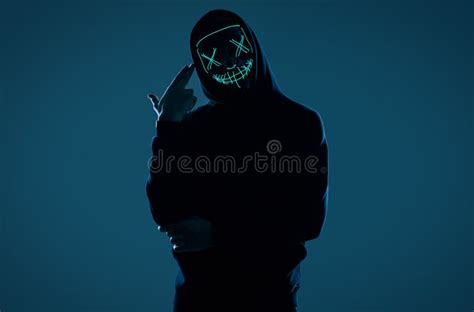 Anonymous Man In Black Hoodie Hiding His Face Behind A Neon Mask Stock