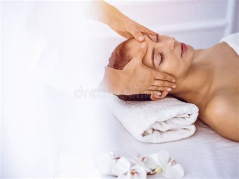 Beautiful Brunette Woman Enjoying Facial Massage With Closed Eyes In Sunny Spa Center Relaxing