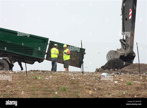Waste Management Landfill Workers With A Backhoe Placing Dirt On Trash